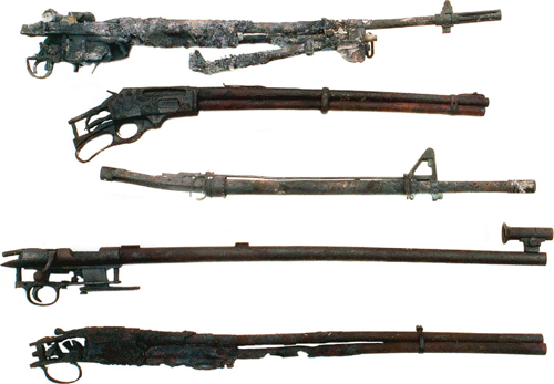 These inoperable sporting arms represent how your arms collection might appear after a house fire. Top to bottom: 1. What was a M14A1 with a bipod and the remains of a scope mount. The scope and much of the mount has melted, the barrel is warped upward, the entire stock assembly has been consumed along with many of the thin metal parts. 2. The Marlin Model 336 appears in better shape than some of the other arms, but the barrel/magazine tube assembly is warped, the stock and forearm are gone, and only the heavy forged steel receiver appears reasonably intact, although the action is inoperable. 3. The barrel of this AR-15 HBAR is slightly warped upward, as is the bolt carrier. However, the aluminum upper and lower receiver units, and synthetic stock and forearm did not fare well. 4. The Remington Model 37 target rifle was a massive design constructed almost entirely of steel and walnut. The stock was consumed, but most of the metal parts survived, even the receiver sight, which is not shown. The heavy barrel is warped slightly downward and to the right. 5. With their thin barrels, side/side and over/under shotguns do not come through house fires as well as pump and auto loading shotguns which tend to have heavier barrels. The barrels of this 20-gauge SKB over/under are literally falling apart, having been burnt through in several places.