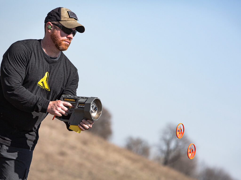 A man launching clays with the Caldwell ClayCopter Hand-Held Thrower while standing in a field.