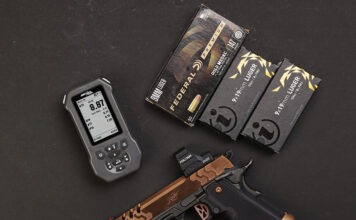 Double Alpha EDGE Shot Timer: The Timer Never Lies The Double Alpha EDGE Shot Timer sitting next to a Kimber pistol and three boxes of ammo on a black background.