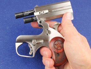 Because of its top hinge, the Bond Arms derringer should be held sideways or slightly inverted to prevent cartridges from sliding out when closing the action. The lever is the barrel release, the auto/manual extractor is mounted on the barrel, and the circular object under the hammer is the cross bolt safety. 