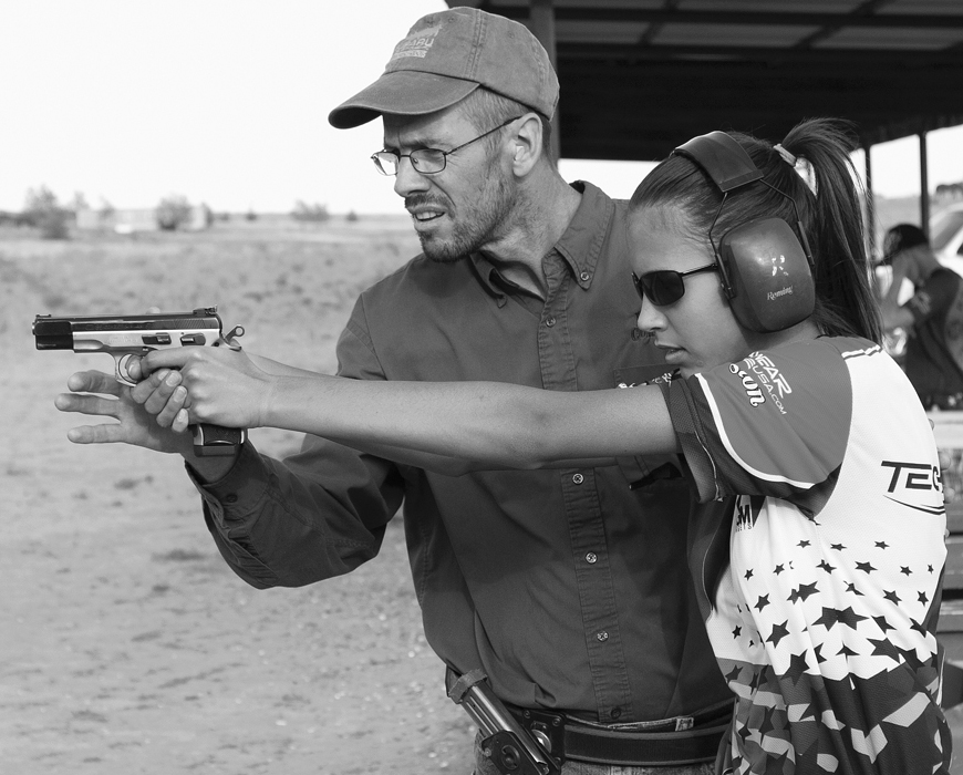 A father pressing the trigger for his daughter to eliminate shooter flinch. He is also able to check for her accuracy of aiming this way.