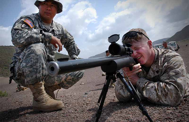 Army Sergeant observes Marine Corps Sergeant, as he fires an M-24 rifle during a familiarization shoot. 