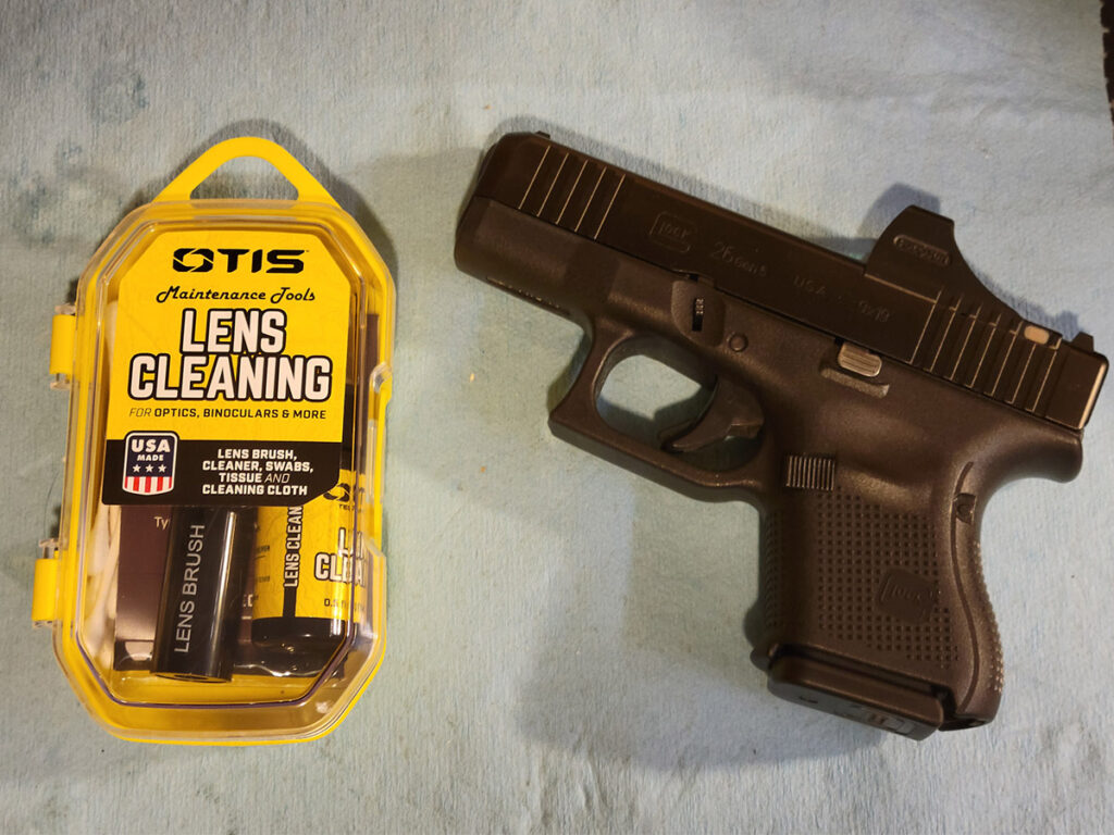 The Otis Lens Cleaning Kit next to a Glock 26 with a Holosun SCS red dot laying on a blue shop towel.