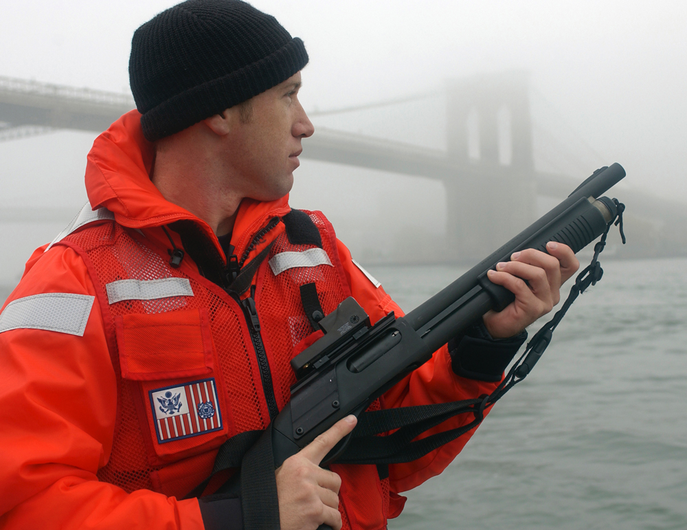 A U.S. Coast Guard petty officer from Maritime Safety and Security Team 91106 armed with an M870P fitted with a Trijicon reflex sight and a Speedfeed stock.