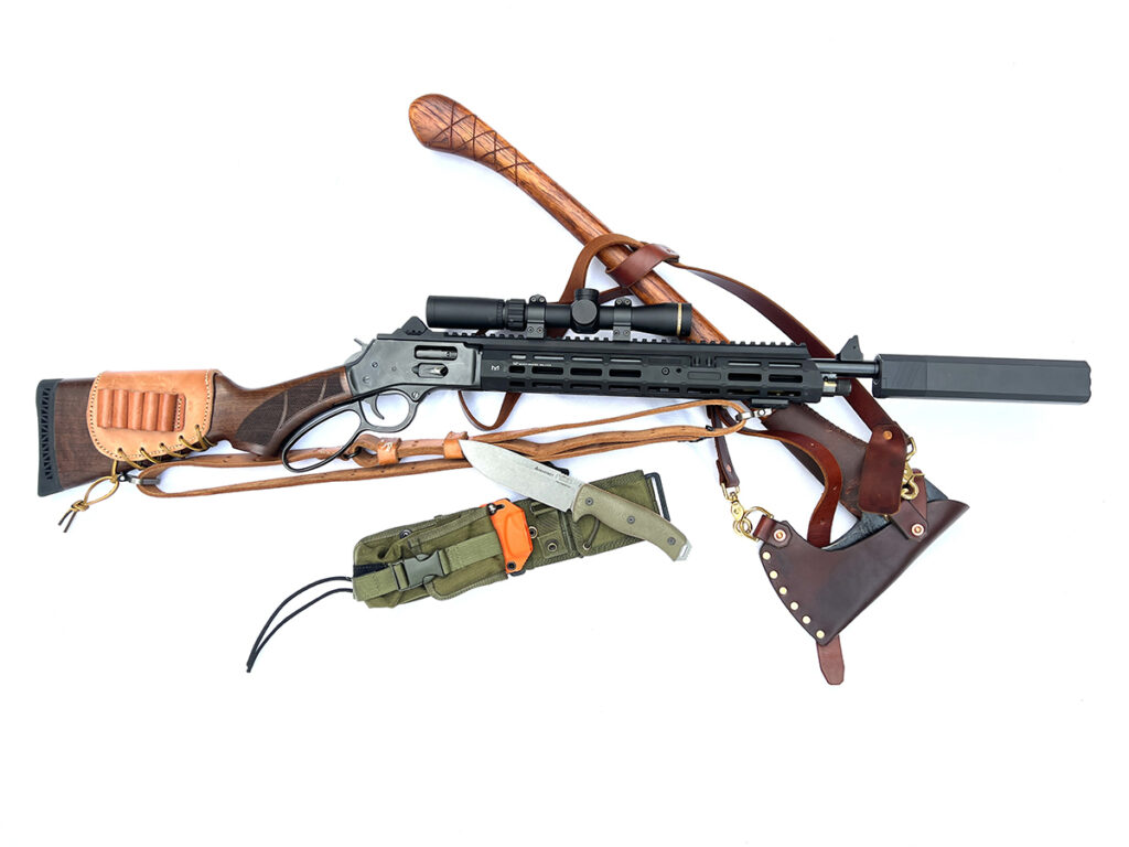 A lever-action brush gun equipped with a scope, suppressor and M-LOK handguard, lying next to a knife and an axe, on a white background.
