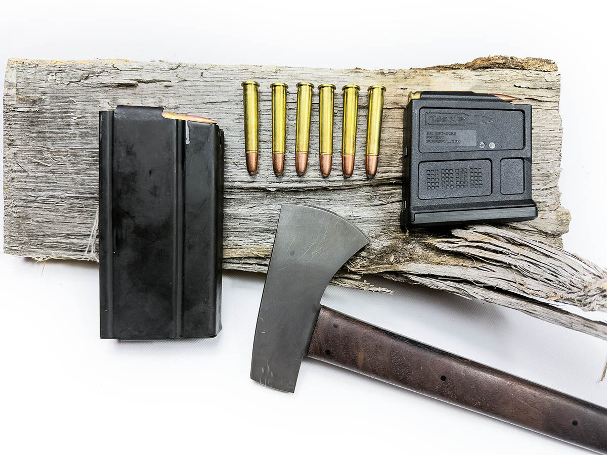 A loaded M14 magazine, six loose .360 Buckhammer rounds, a loaded AICS magazine and a tomahawk laying on a log.