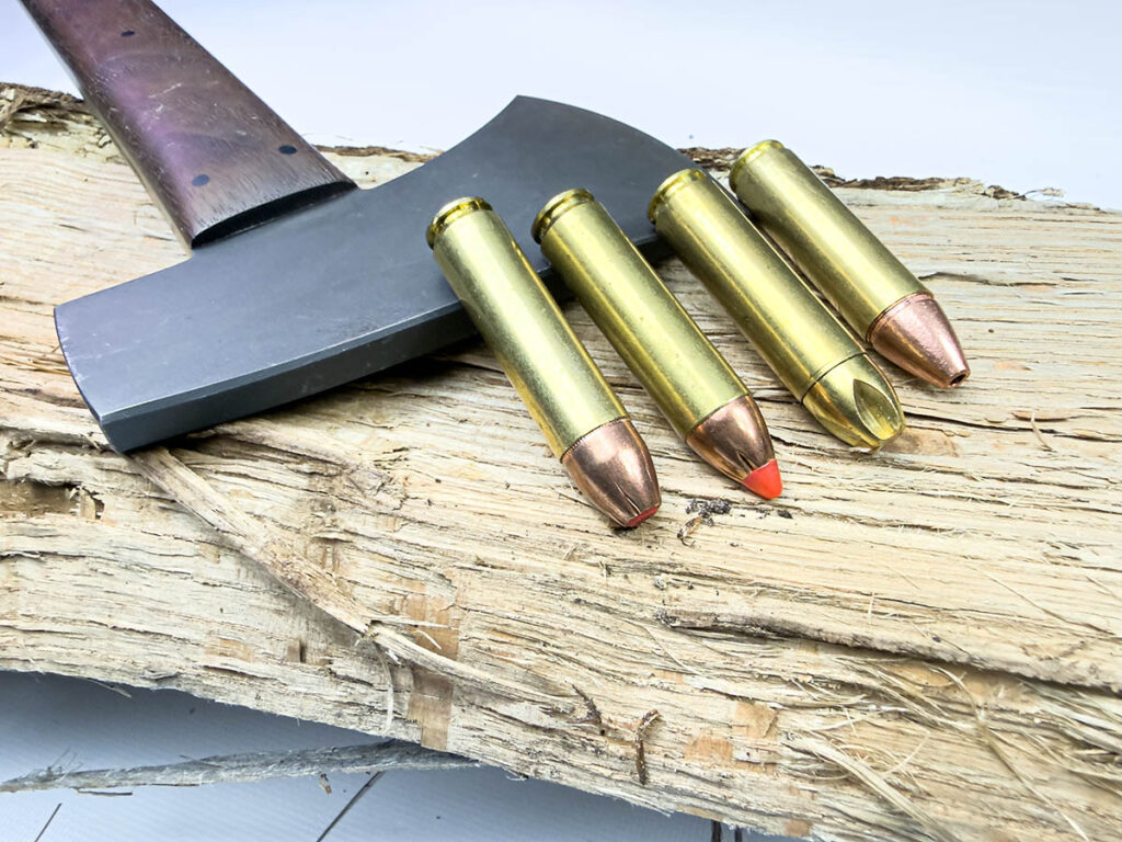 Four different .450 Bushmaster cartridges laying on a tomahawk blade on a log.