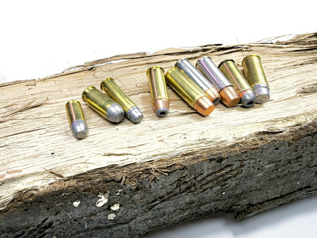 A spread of different handgun cartridges lying on a log.